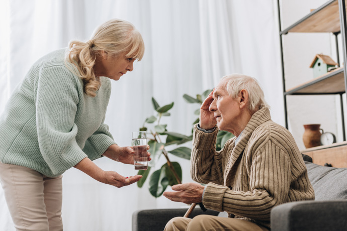 Mujer dando vaso de agua a hombre con Alzheimer.