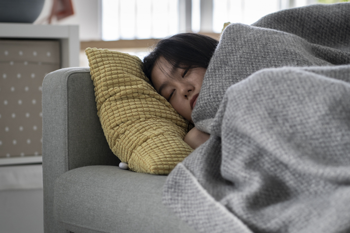 Mujer durmiendo en sofá arropada con manta que sufre escalofríos sin fiebre.