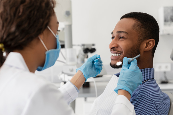 Dentista revisando si un hombre toma vitaminas para fortalecer sus dientes.