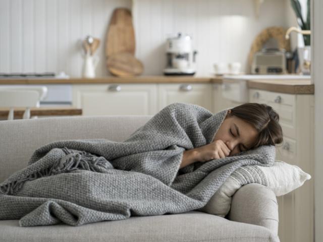 Mujer tumbada en el sofá tapada con manta que sufre escalofríos sin fiebre.