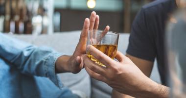 Persona con intolerancia al alcohol rechazando con la mano un vaso de licor